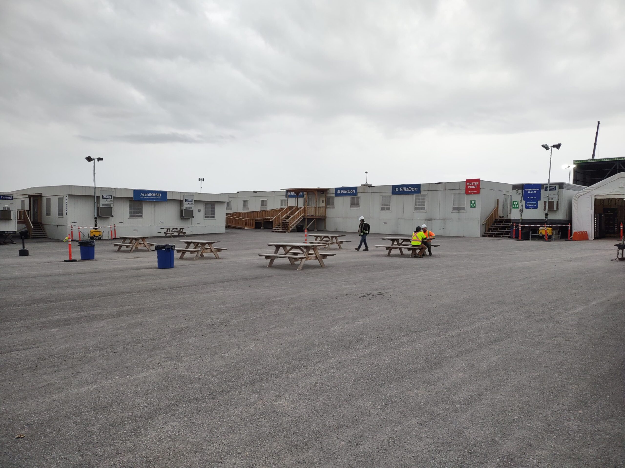 Industrial light towers illuminating a construction jobsite with temporary site buildings and workers