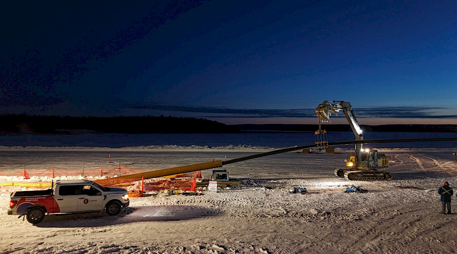 Cranes and excavators lifting pipeline section at sunset on frozen lake in Alberta