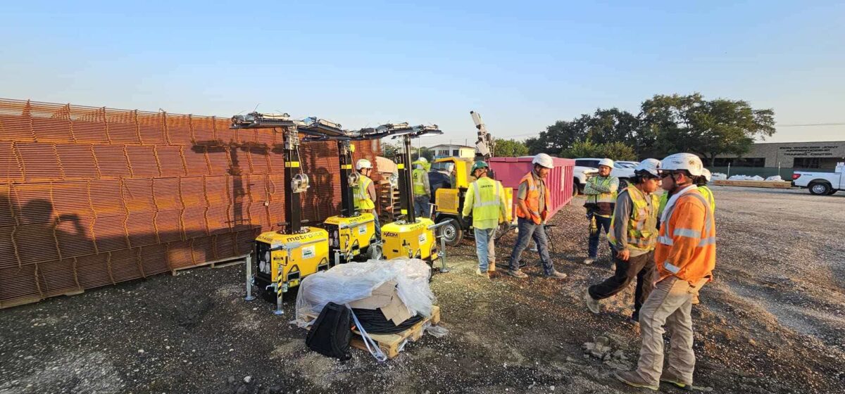 Granite Construction crews standing beside hybrid light towers during daytime setup at a Houston airport project site.