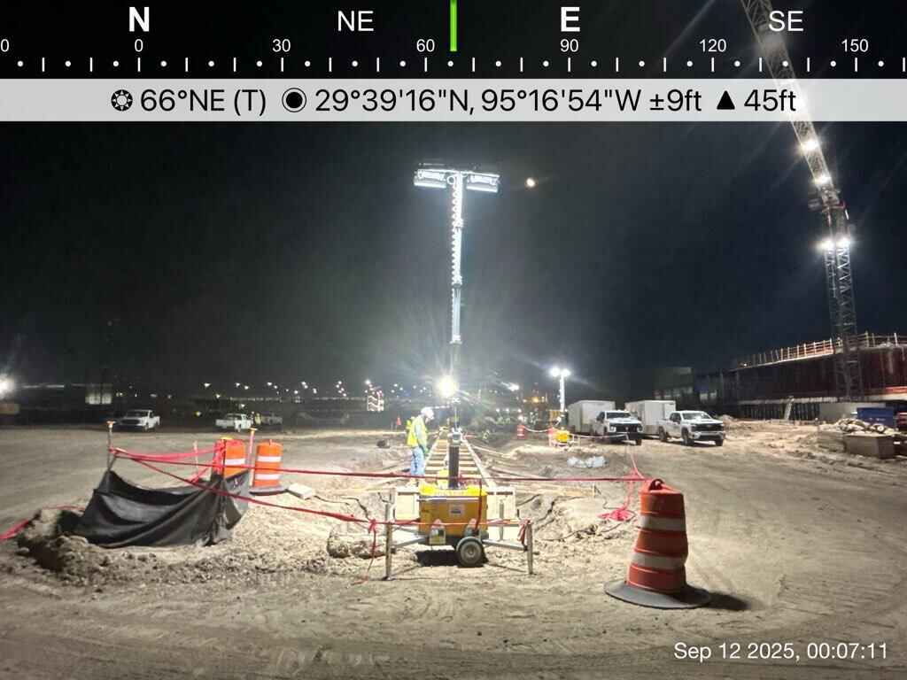Wide view of a Houston airport construction worksite illuminated by a hybrid light tower during nighttime concrete work.